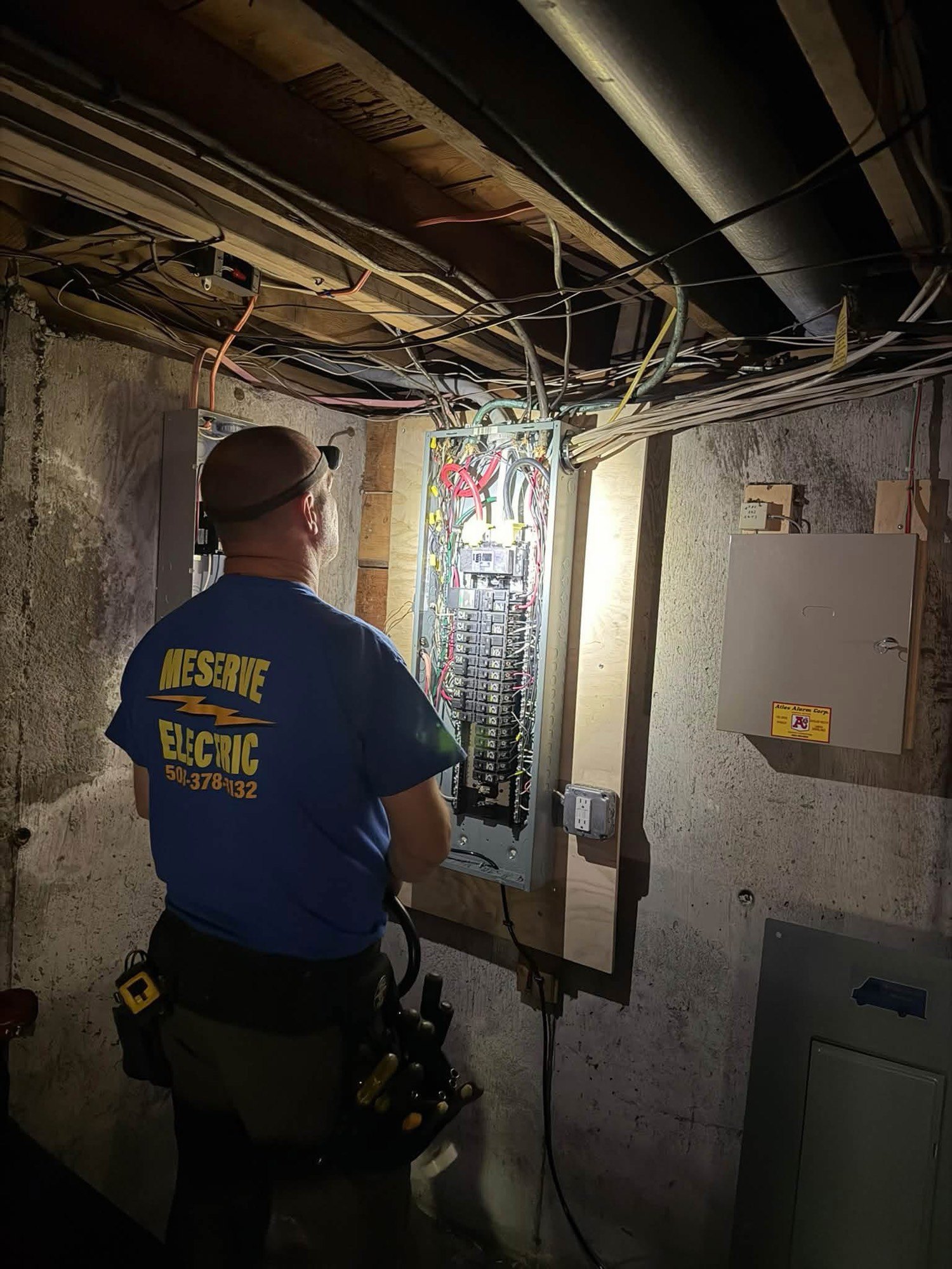 Jason Meserve, in a Meserve Electric shirt, working at an open electrical panel